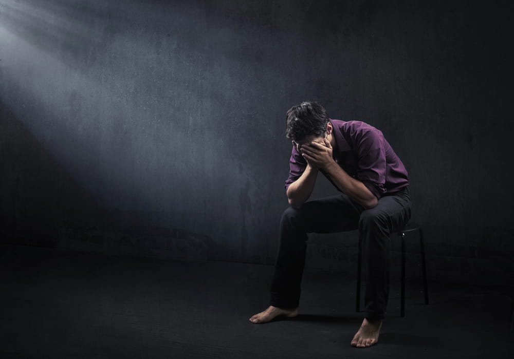 Image is of a distressed man sitting alone with his face covered in a dark room, concept of sex crime allegations and the emotional impact false accusations may have on an individual.