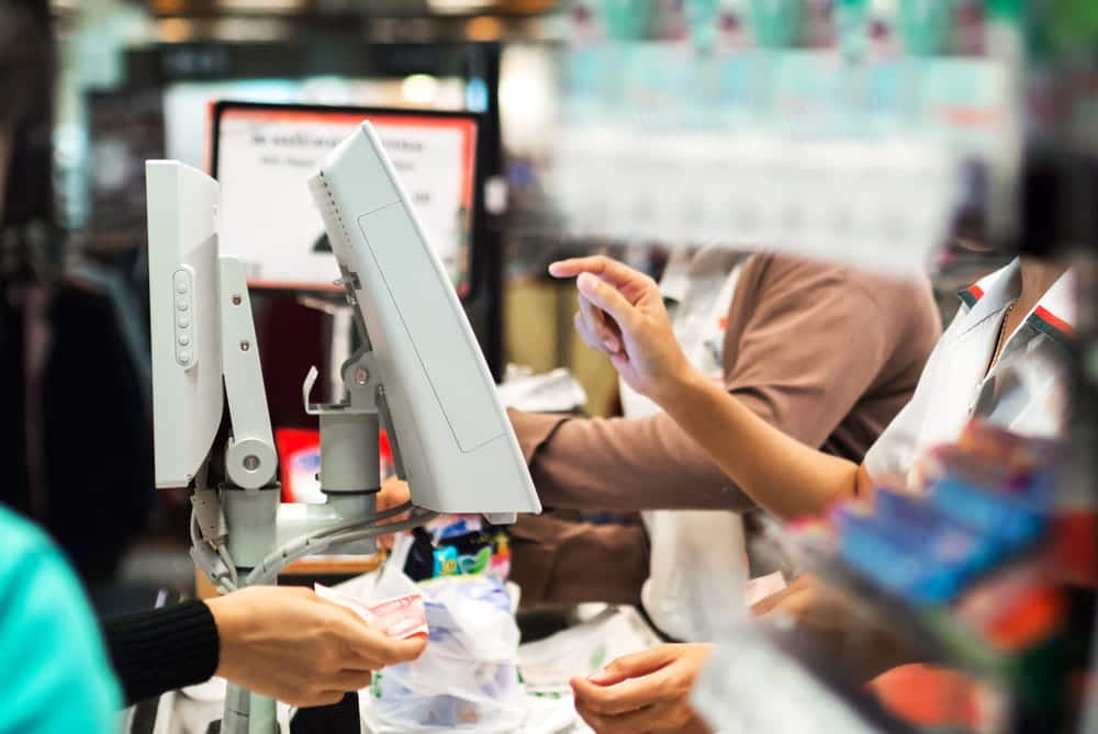 Image is of retail employees working at a checkout counter during a store transaction, concept of a theft charge and reviewing purchase records during a theft investigation.