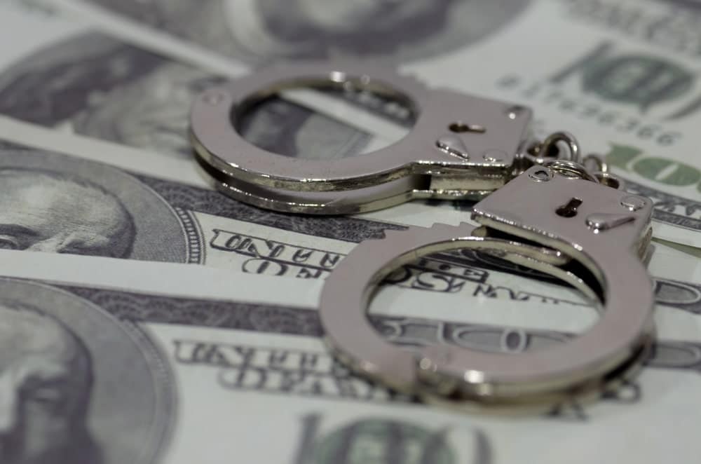 Image is of handcuffs placed on dollar bills, concept of financial consequences connected to an arson lawyer