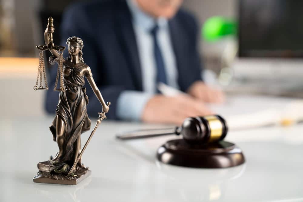 Image is of a lawyer working beside a courtroom gavel and Lady Justice statue, concept of an auto theft lawyer handling criminal defense matters.