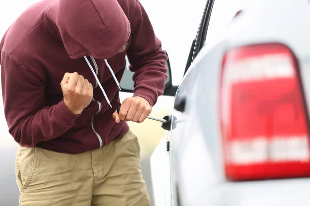 Image is of an individual attempting to break into a parked vehicle, concept of an auto theft lawyer handling vehicle theft accusations.