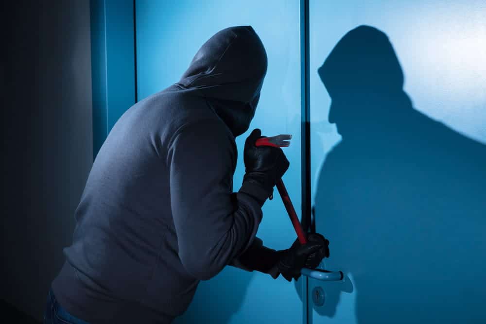 Image is of a masked individual attempting forced entry into a property, concept of a burglary lawyer handling burglary-related accusations.