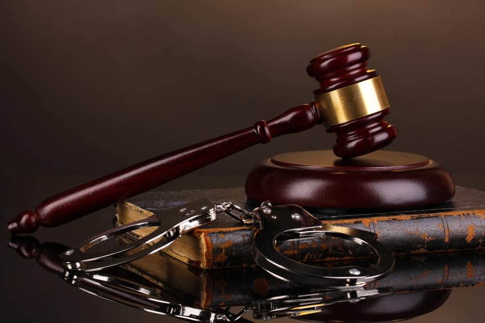 Image is of a courtroom gavel and handcuffs placed on legal books, concept of a burglary lawyer defending felony allegations.