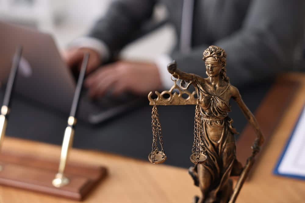 Image is of a lawyer working at a desk beside a Lady Justice statue, concept of a burglary lawyer handling criminal defense matters.