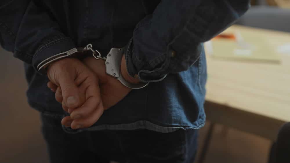 Image is of a person in handcuffs during an arrest investigation, concept of a criminal defense lawyer handling criminal charges in Clinton