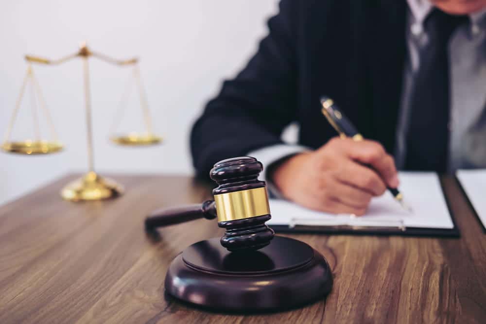 Image is of an attorney writing legal notes beside a courtroom gavel, concept of a criminal defense lawyer handling court proceedings