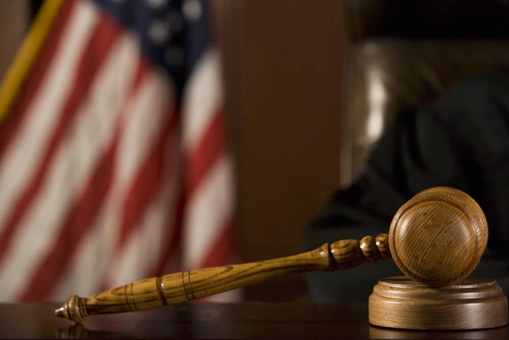 Image is of a judge’s gavel placed on a desk with an American flag in the background, concept of domestic violence lawyer