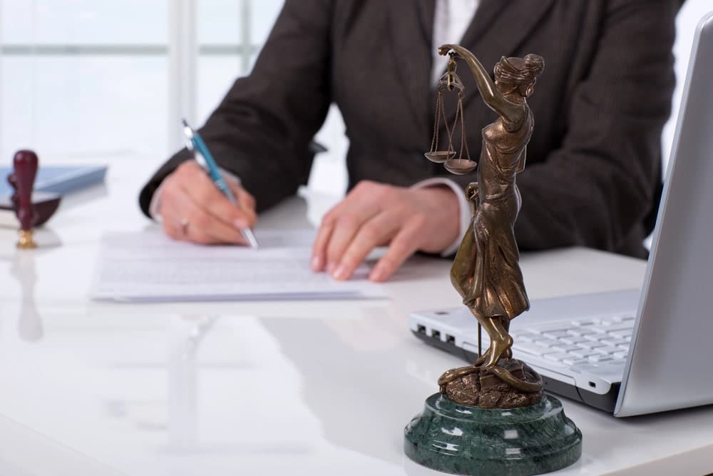 Image is of a lawyer reviewing documents beside a Lady Justice statue, concept of domestic violence lawyer