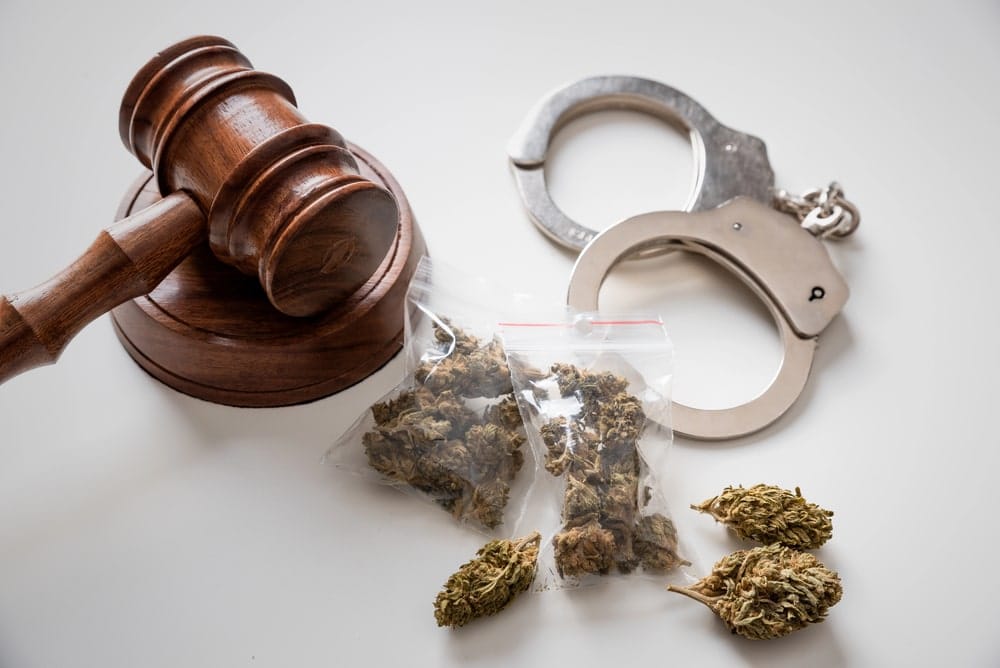 Image is of a gavel and handcuffs placed beside seized drugs on a surface, concept of drug crimes lawyer