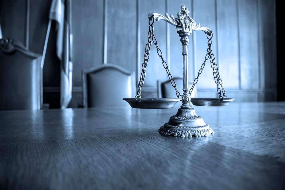 Image is of scales of justice in a courtroom setting, concept of drug distribution lawyer evaluating evidence and legal balance