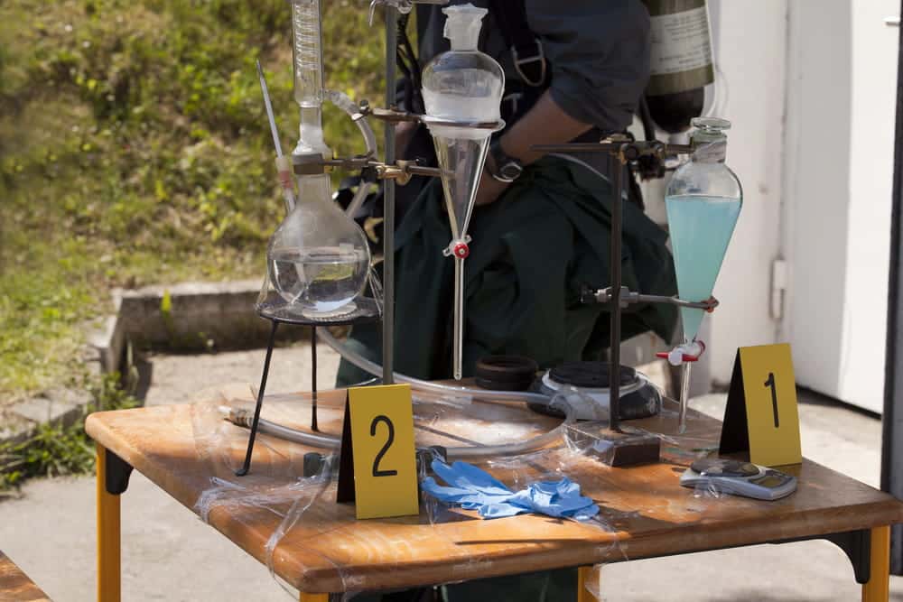 Image is of a hazmat team examining drug lab equipment with evidence markers, concept of drug manufacturing lawyer reviewing investigation details