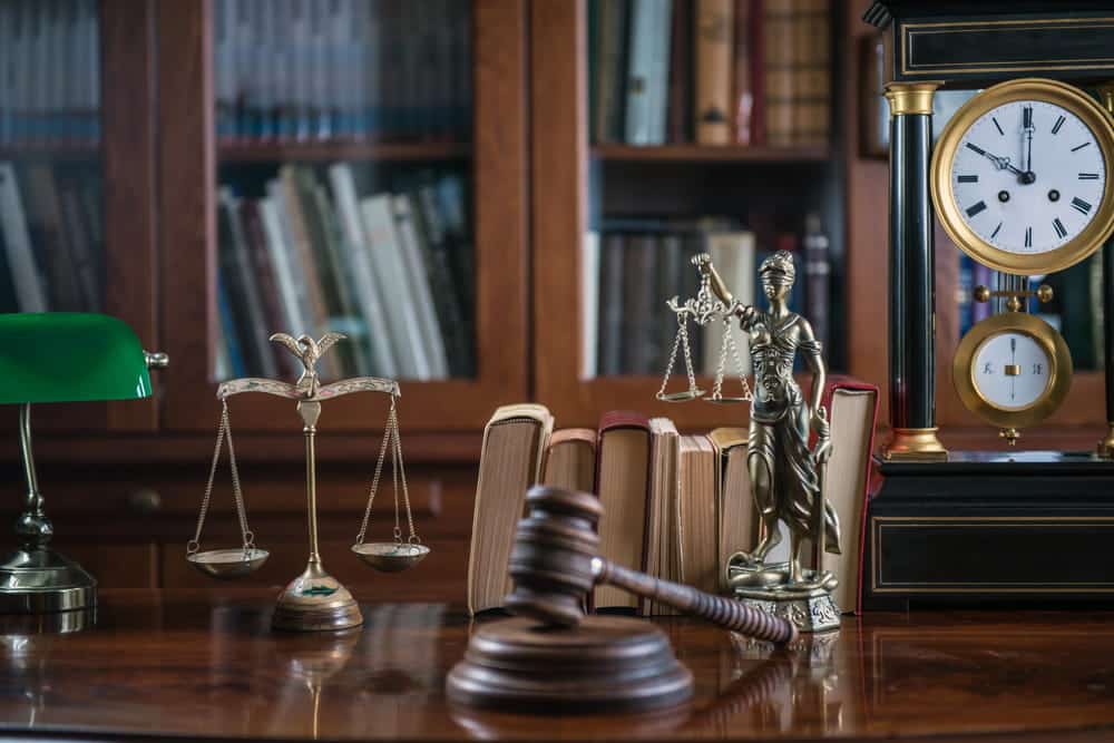 Image is of a law office desk with gavel, scales, and legal books, concept of drug manufacturing lawyer handling complex charges