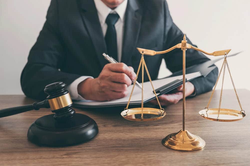 Image is of a lawyer signing documents with a gavel and scales on a desk, concept of drug possession lawyer preparing a defense strategy