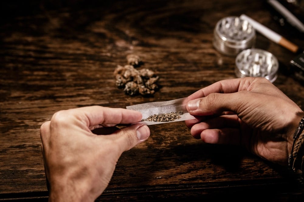 Image is of a person preparing marijuana on rolling paper, concept of drug trafficking lawyer reviewing substance related evidence