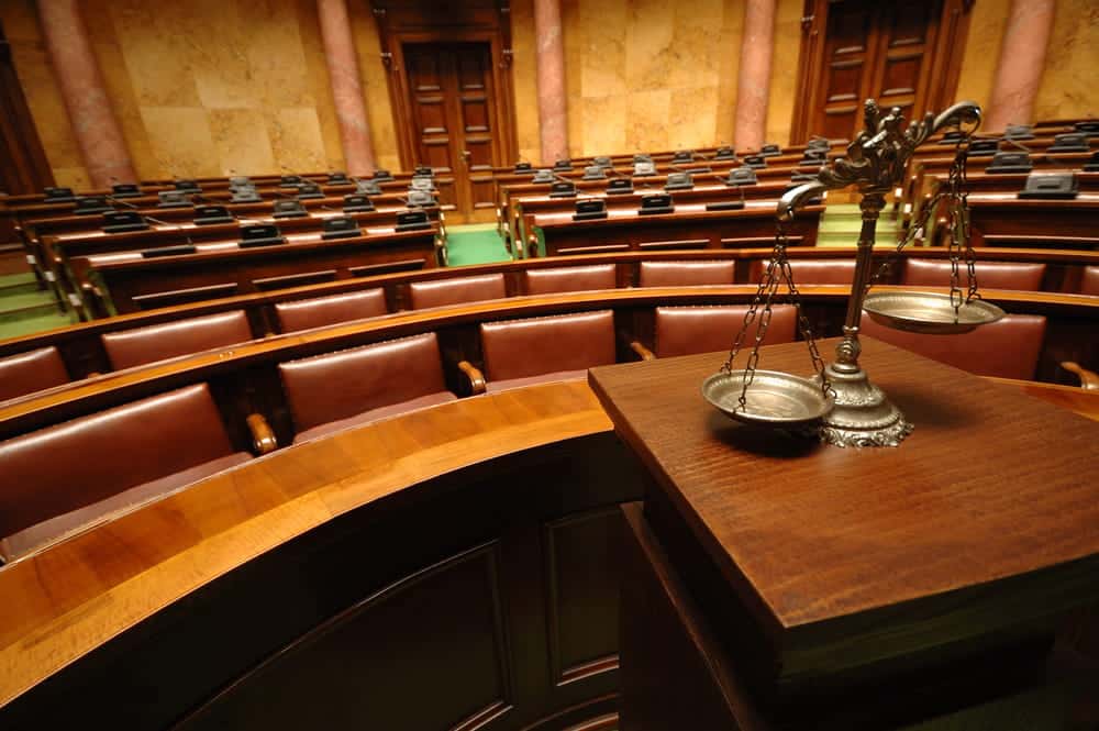 Image is of a courtroom with seating and a justice scale displayed, concept of gun crimes lawyer