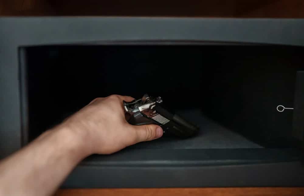 Image is of a person placing a handgun inside a safe, concept of gun crimes lawyer