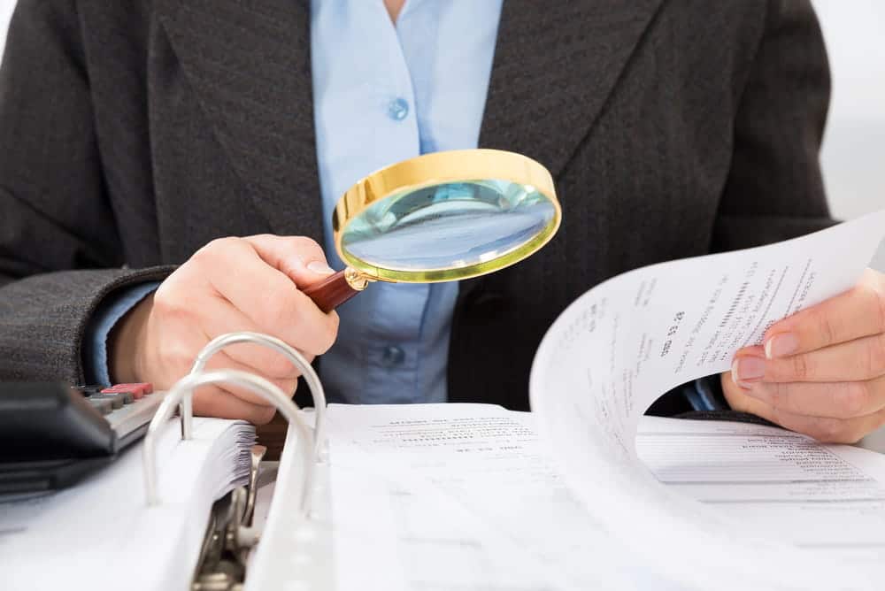 Image is of a person reviewing paperwork with a magnifying glass, concept of home improvement fraud lawyer.