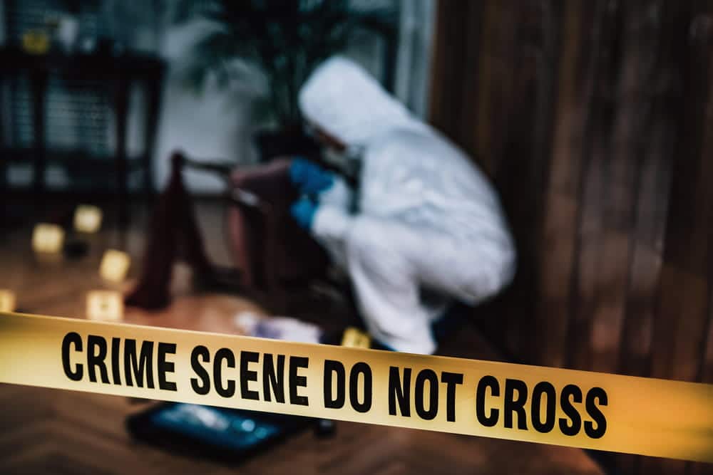 Image is of a forensic investigator working behind crime scene tape, concept of murder defense lawyer