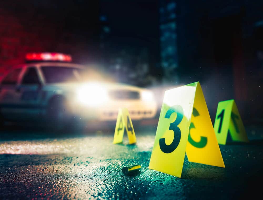 Image is of evidence markers placed near a bullet casing with police lights in the background, concept of murder defense lawyer