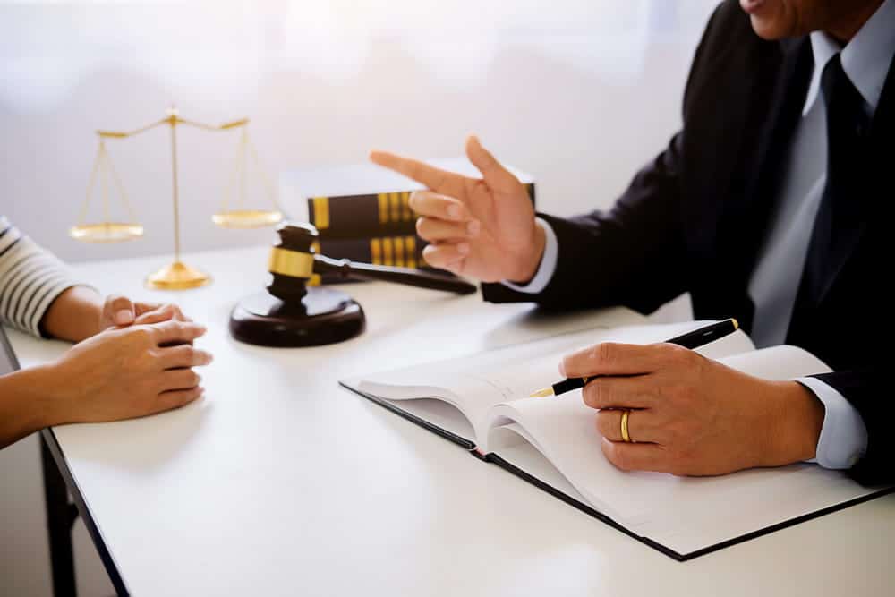 Image is of a lawyer pointing during a discussion with a client near scales and a gavel, concept of rape defense lawyer building a defense strategy