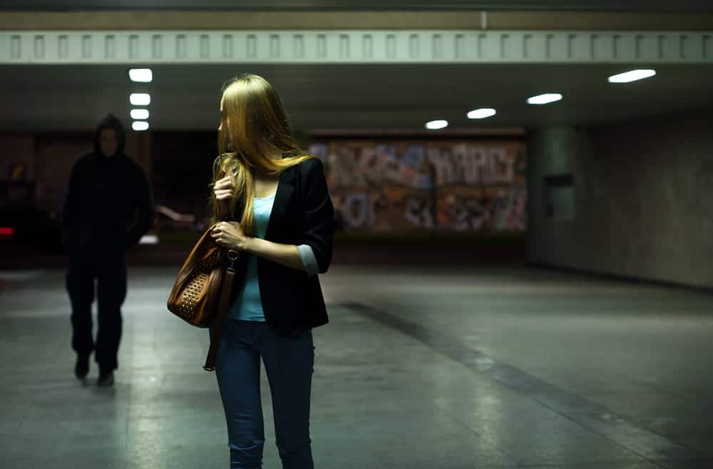 Image is of a woman walking through a dimly lit area while being followed, concept of a robbery lawyer handling violent crime accusations.