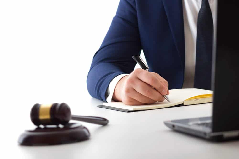 Image is of a lawyer writing legal notes beside a courtroom gavel, concept of a robbery lawyer preparing a criminal defense case.