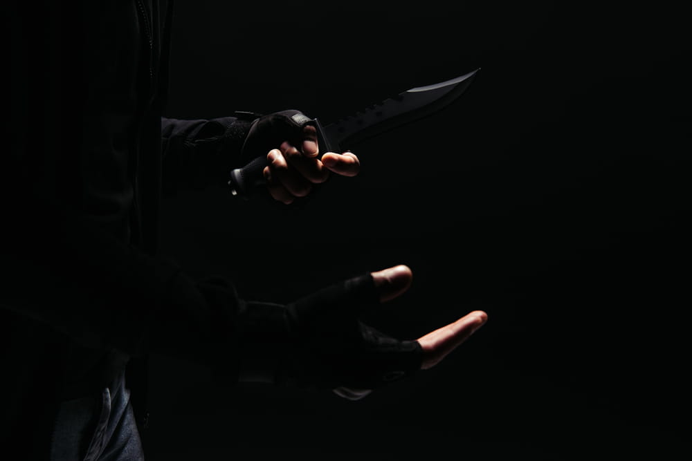 Image is of a person holding a knife in a dark setting, concept of a robbery lawyer defending weapon-related robbery accusations.