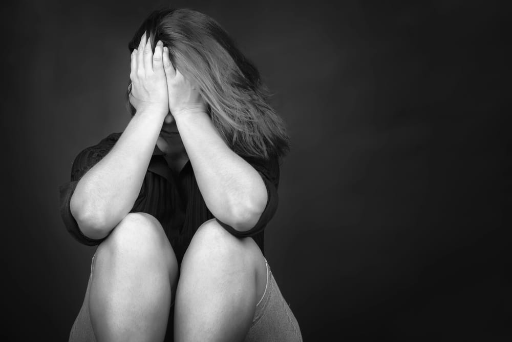 Image is of a person sitting with their face covered in distress, concept of sex crimes lawyer addressing serious allegations and impact