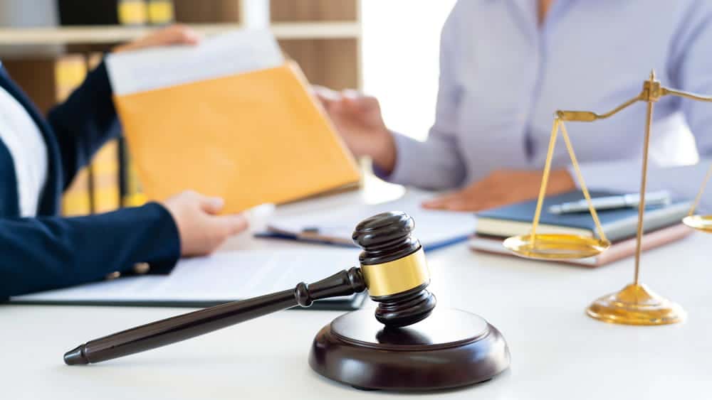 Image is of a lawyer handing legal documents across a desk with a gavel and scales visible, concept of sexual assault lawyer reviewing case evidence