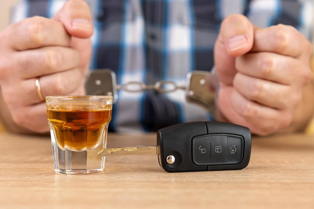 Image is of handcuffs, car keys, and a glass of alcohol on a table, concept of Knoxville DUI defense lawyer.