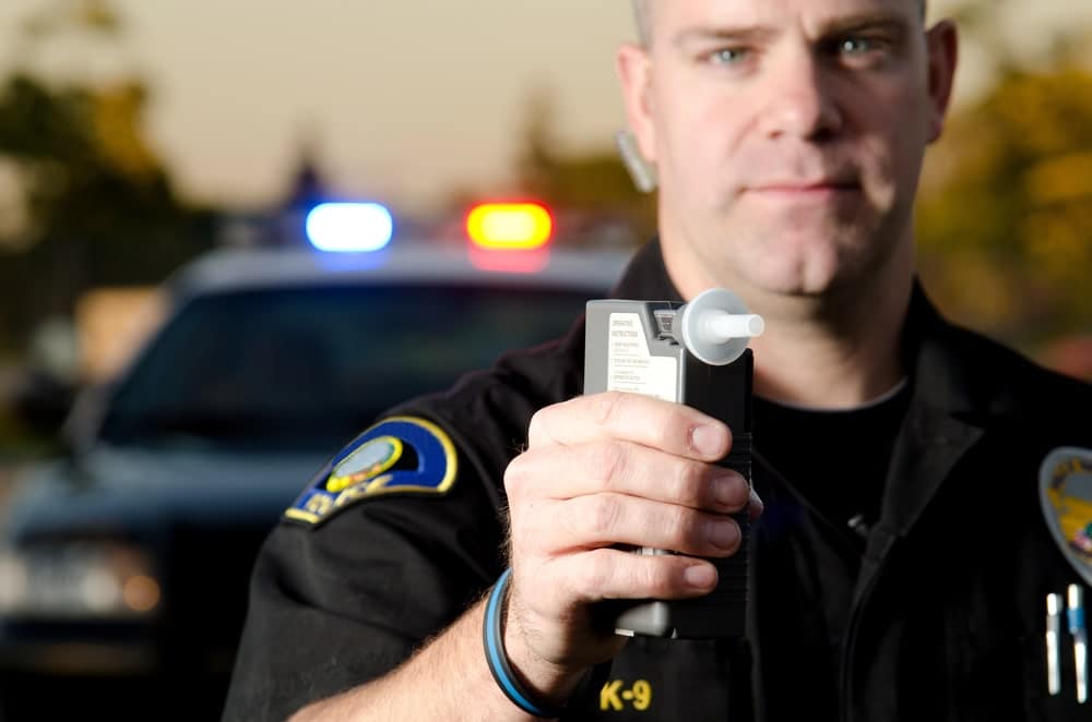 Image is of a police officer holding a breath test device near a patrol car, concept of Knoxville DUI defense lawyer.