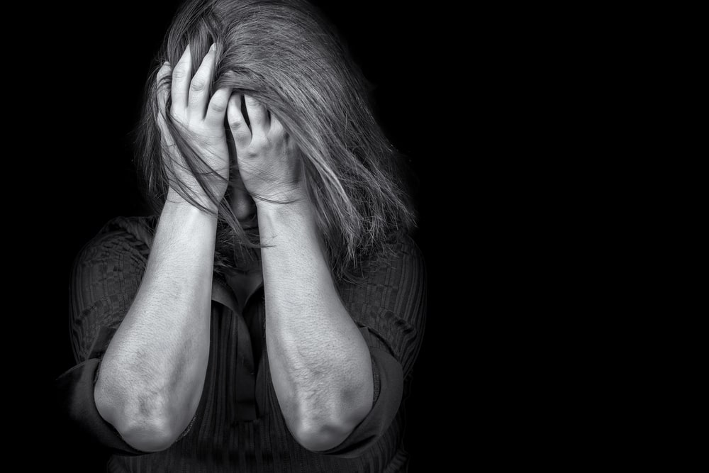 Image is of a distressed woman covering her face, concept of Knoxville domestic violence lawyer.