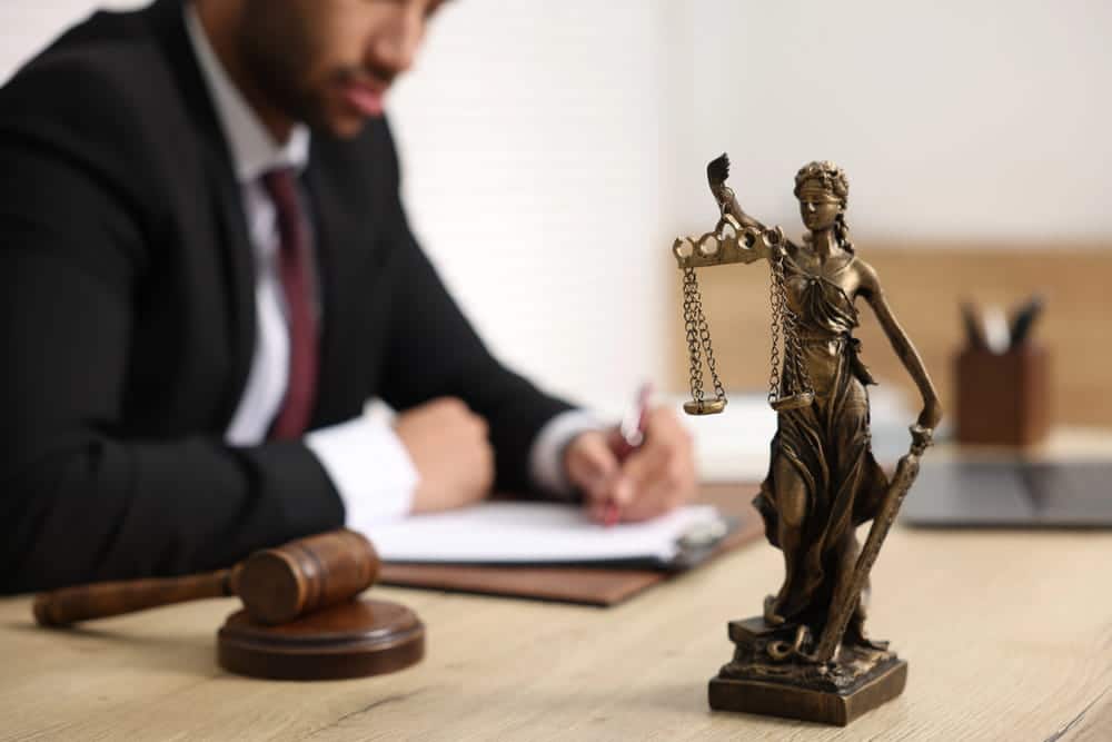 Image is of a lawyer reviewing case paperwork beside a justice statue, concept of Knoxville drug crimes lawyer.