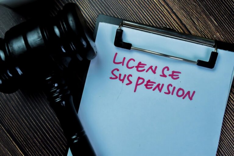 Image is of a clipboard beside a judge’s gavel with the words license suspension written on paper, concept of DUI in Clinton and the risk of losing driving privileges after an arrest.