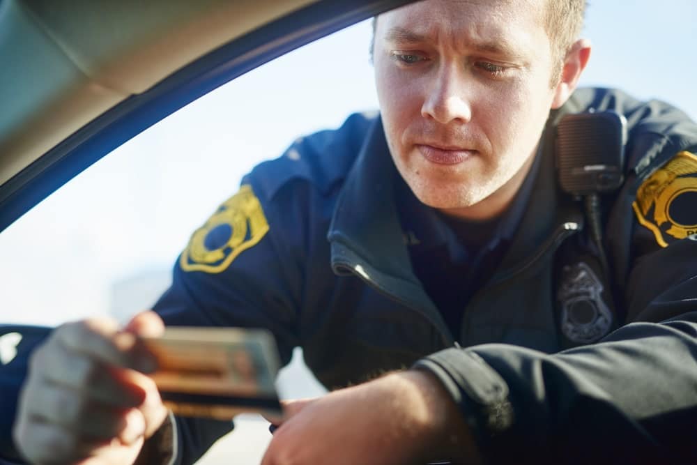 Image is of a police officer reviewing a driver's license during a traffic stop, concept of DUI checkpoints and roadside screening procedures in Knoxville.