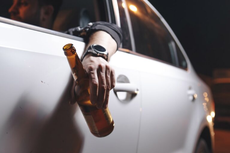 Image is of a driver holding a beer bottle outside a vehicle window, concept of Underage DUI violations and impaired driving offenses in Tennessee.