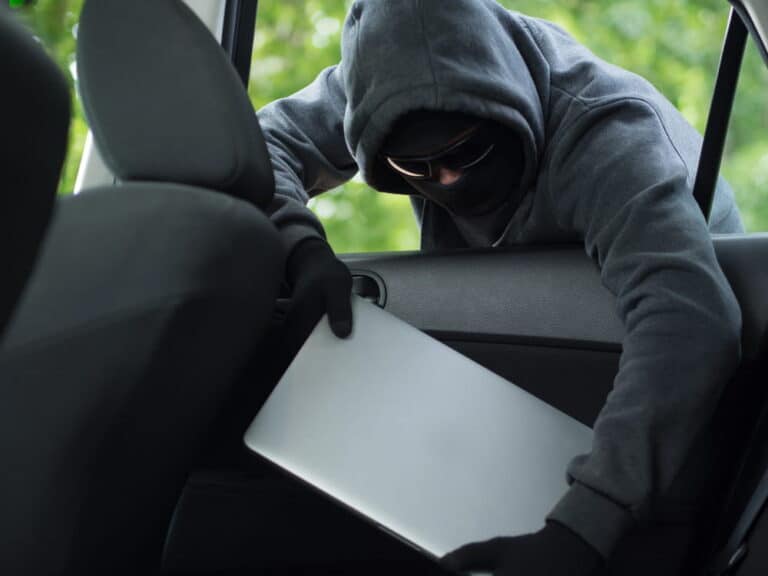 Image is of a person removing a laptop from a parked vehicle, concept of theft under Tennessee law involving unlawful taking of personal property.