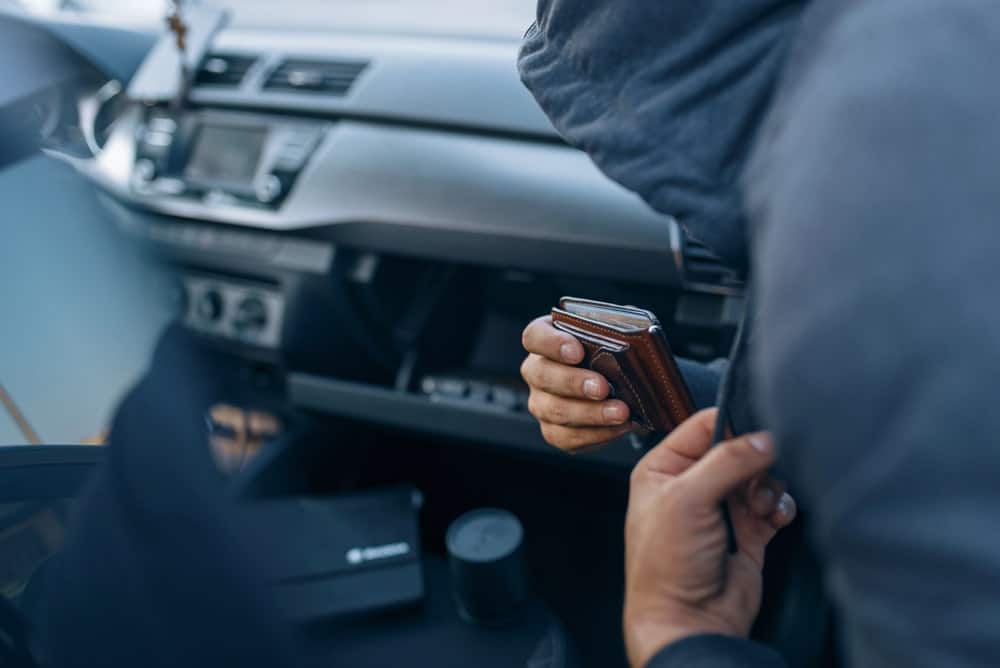 Image is of a person concealing a wallet inside a vehicle, concept of theft under Tennessee law involving unlawful control of another person's property.