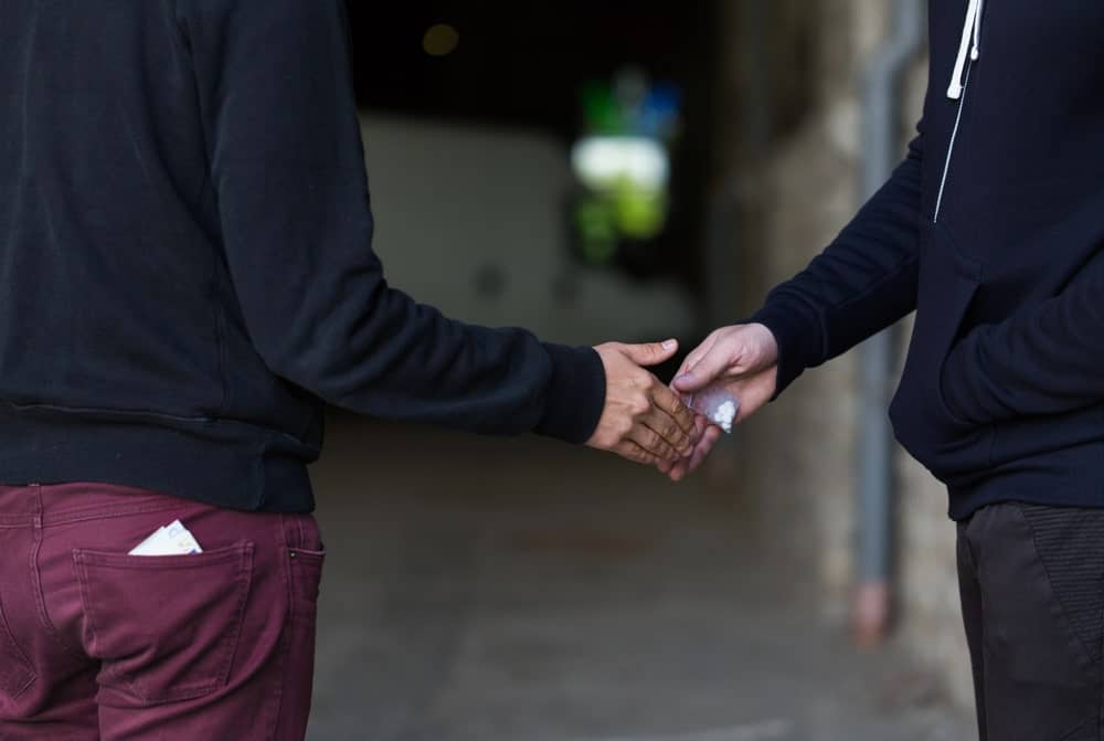 Image is of two people exchanging suspected illegal substances, concept of drug distribution under Tennessee law.