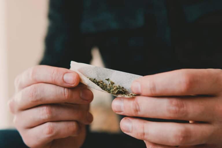 Image is of a person holding a rolled controlled substance, concept of drug possession.