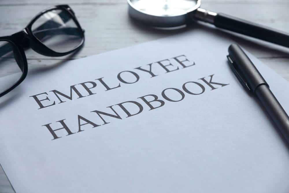 Image is of an employee handbook with a magnifying glass and pen, concept of how a DUI affect employment under workplace policies.