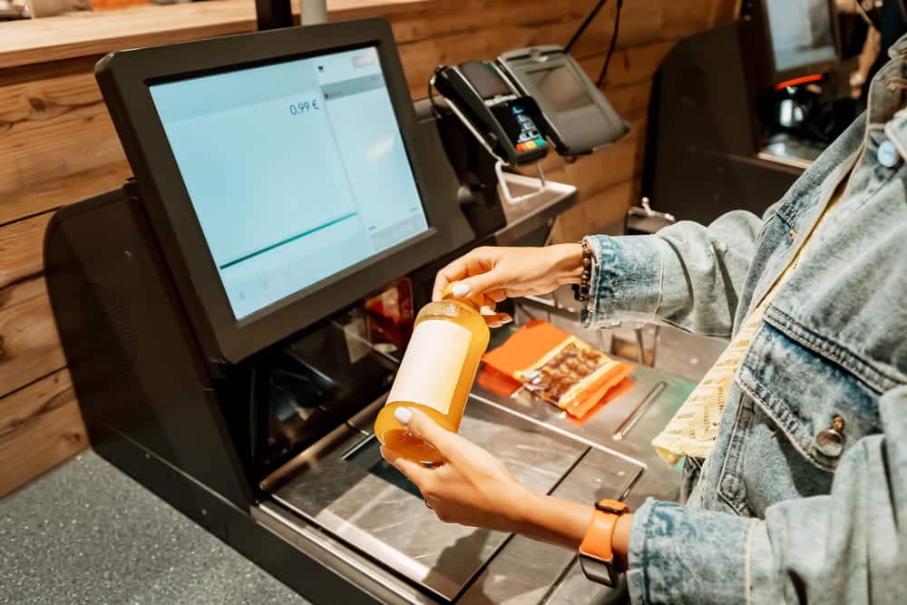 Image is of a shopper handling merchandise at a self checkout station, concept of shoplifting under Tennessee law