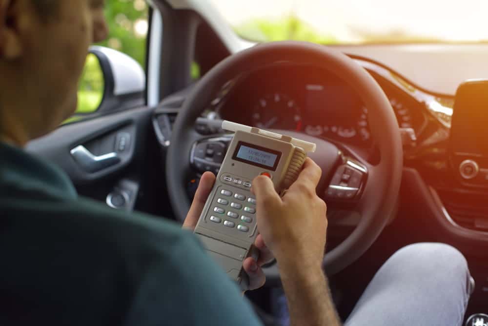 Image is of a driver using a breath testing device inside a vehicle, representing ignition requirements and felony DUI penalties in Tennessee