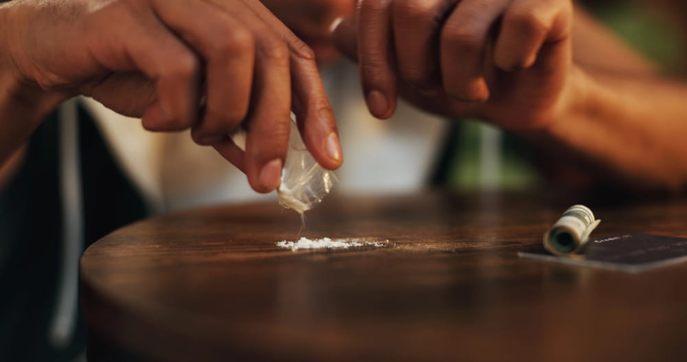 Image is of hands handling a small plastic bag containing white powder on a table, concept of suspected drug evidence investigated in a drug manufacturing charge in Clinton.